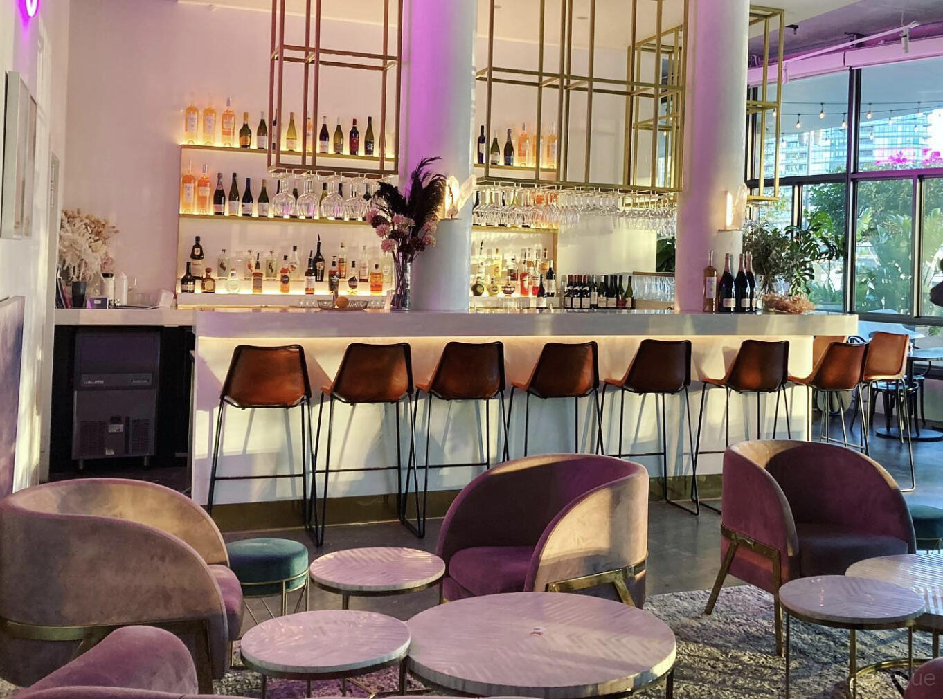 A cafe in a restaurant with a marble-topped bar, leather bar stools, and wall-mounted shelves of bottles at The Espressonist.