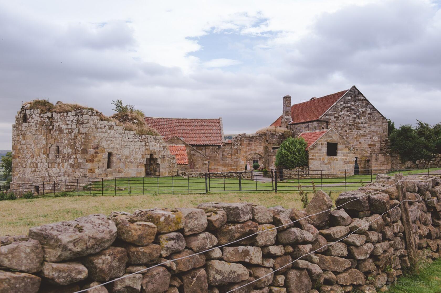 A stone castle with weathered walls, red-tiled roofs, and surrounding lawn at Danby Castle.