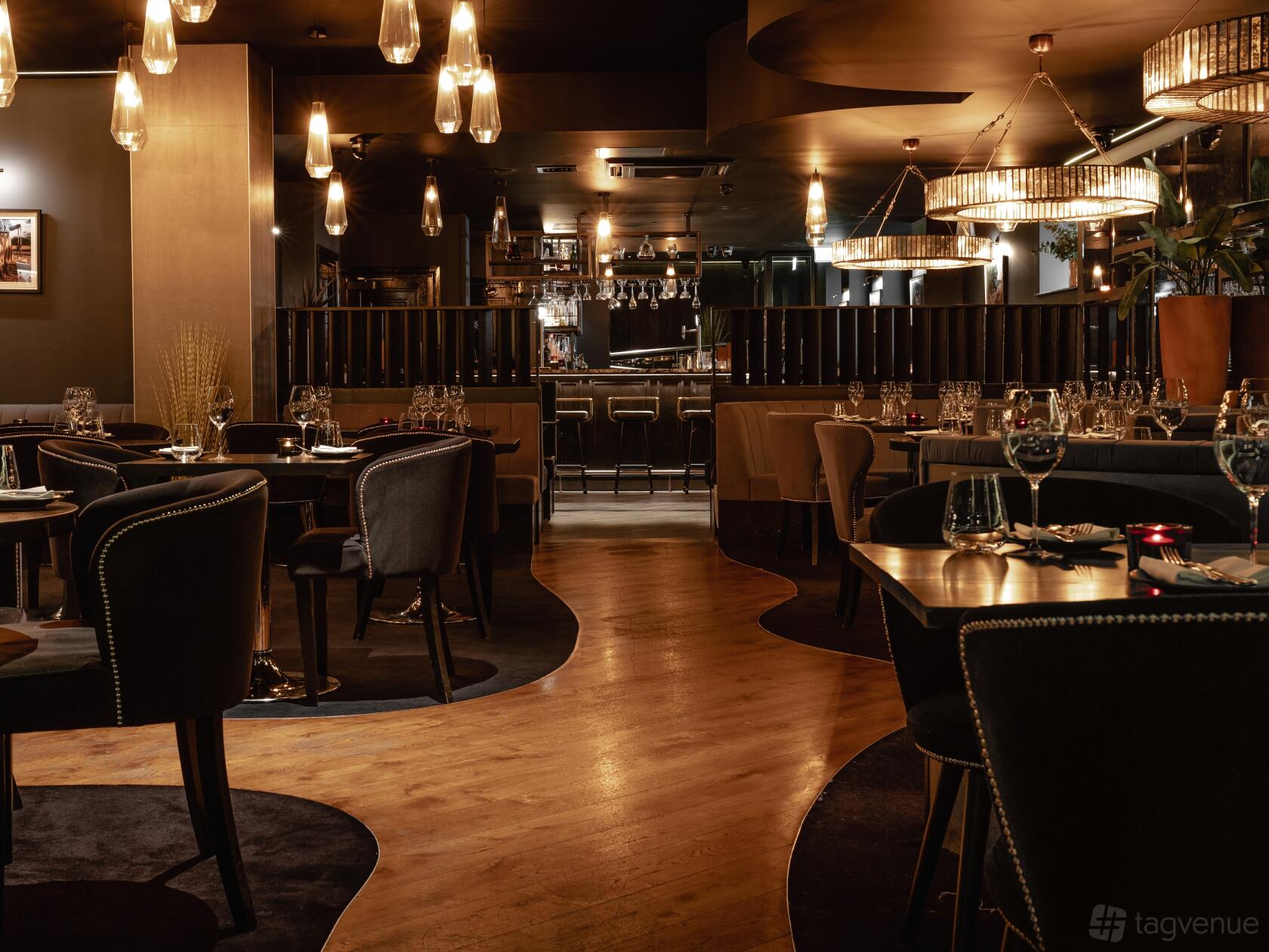 A restaurant with dark upholstered chairs, wood flooring, pendant lighting, and set tables at Gaucho Birmingham.
