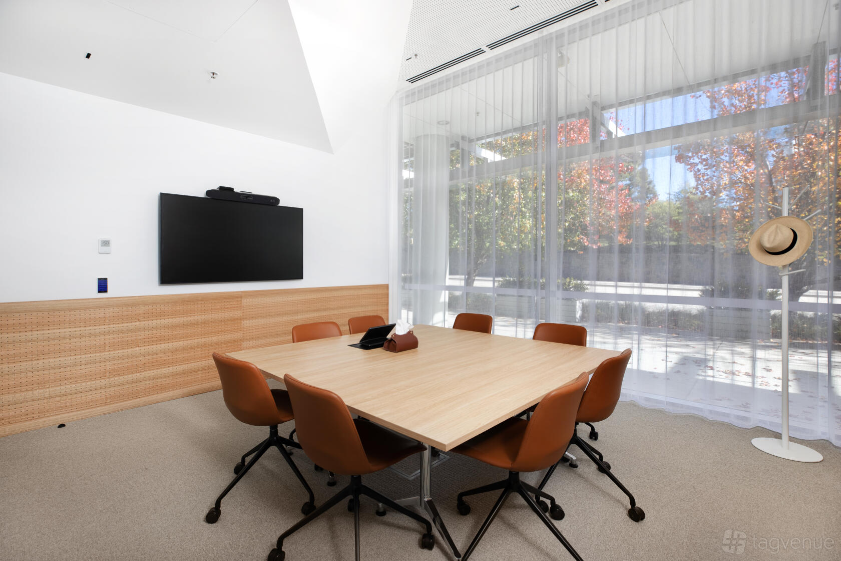 A meeting room with a wooden conference table, brown chairs, wall-mounted screen, and floor-to-ceiling windows at Flex by ISPT Pathway Place.