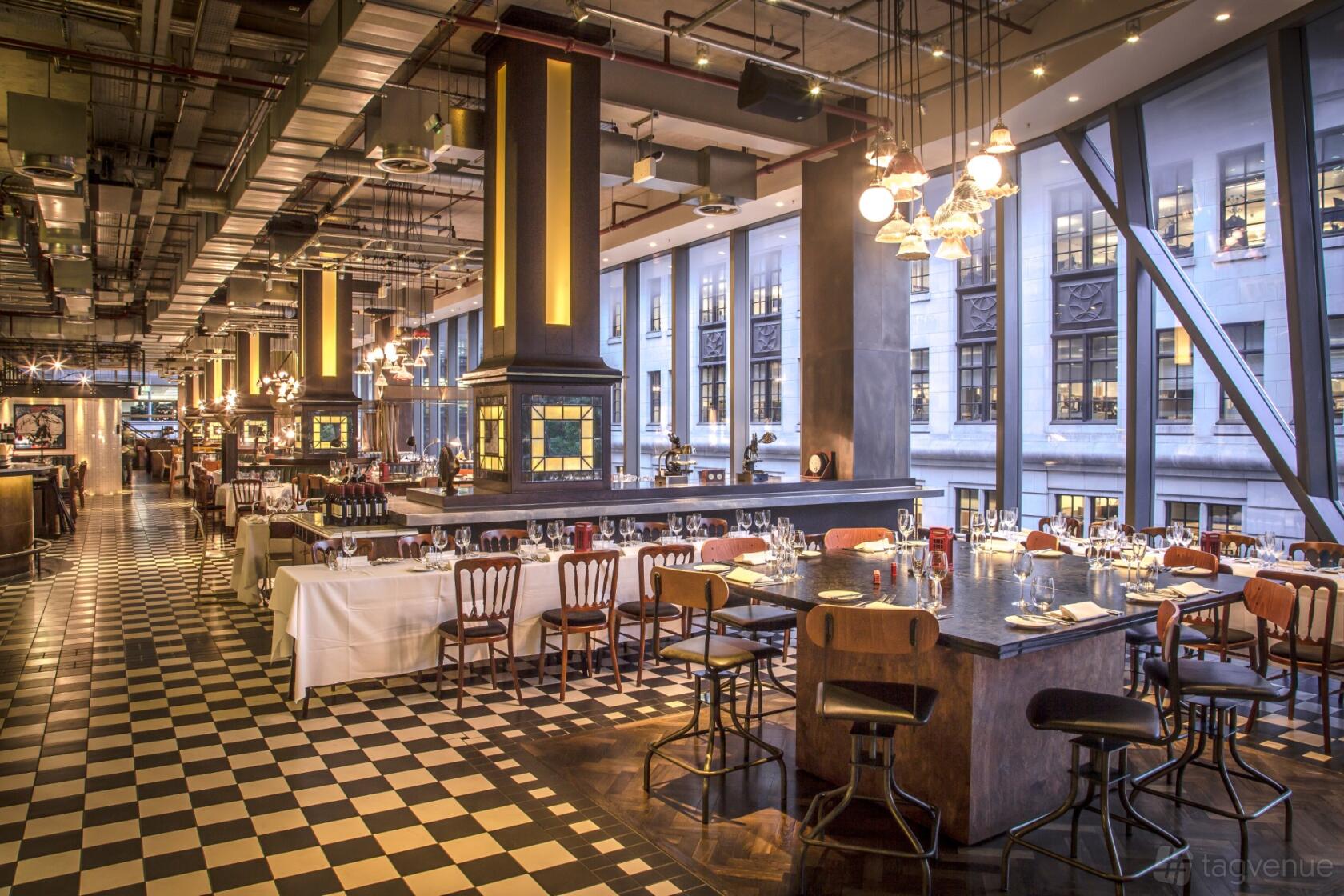A restaurant with floor-to-ceiling windows, checkered flooring, and set dining tables at Bread Street Kitchen, St Paul's.