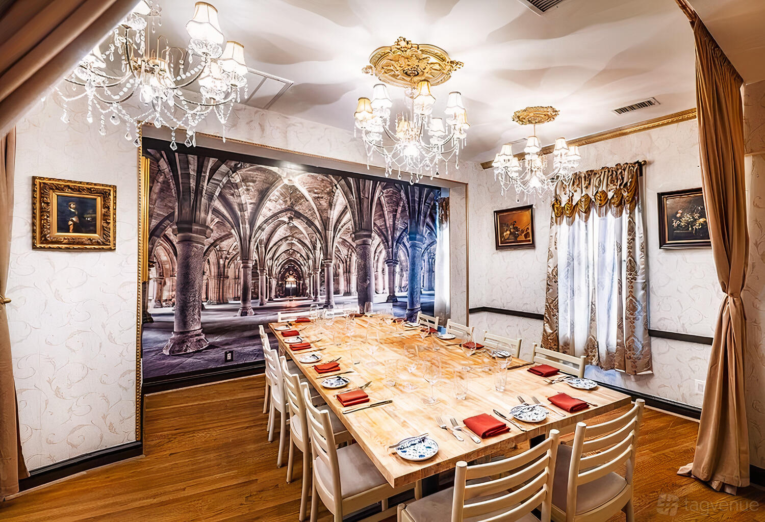 A dining room with a long wooden table, red napkins, chandeliers, and an arched mural at Bistro Cacao.