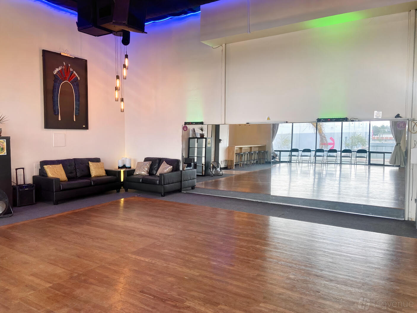 A dance studio with a wood floor, wall-length mirrors, black sofas, and pendant lights at La Vie Dance & Culture.