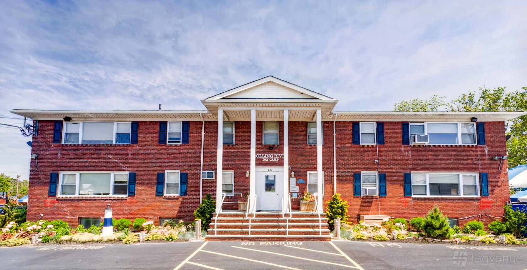 A brick building with white columns, blue shutters, and landscaped entrance at Rolling River Day Camp.