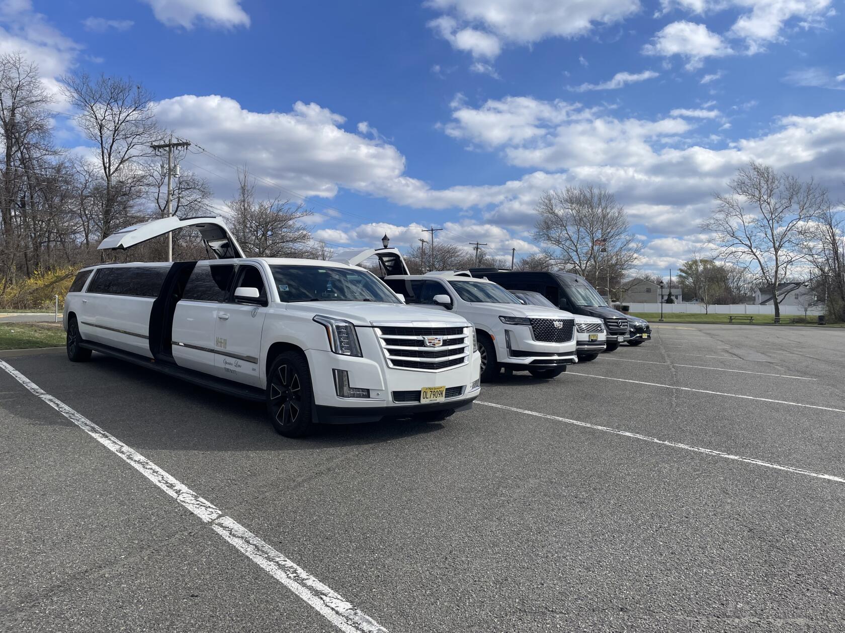 A line of white stretch limousines with upper doors open in a parking lot at NY City Limo Company Limo-house.