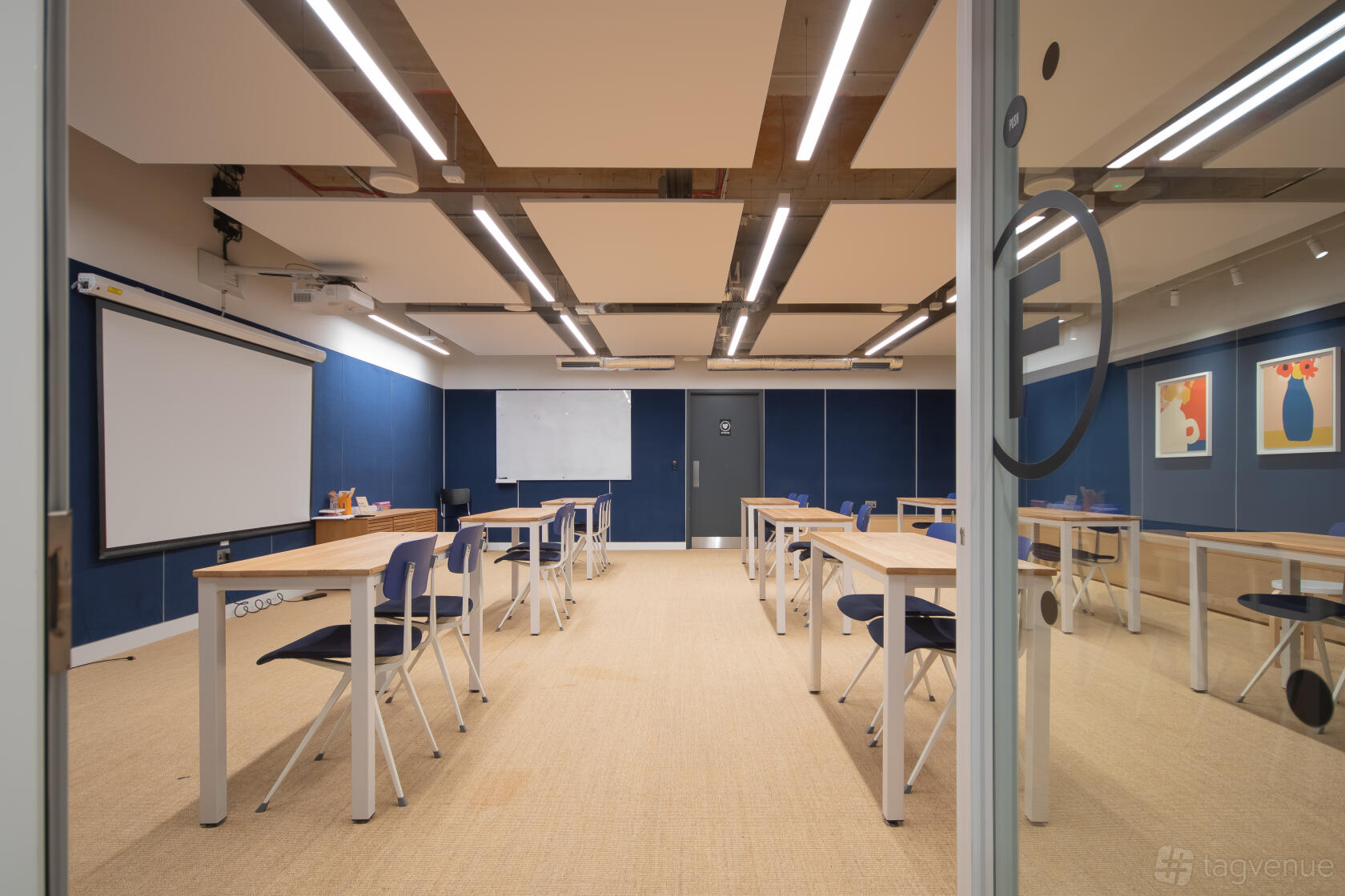 A classroom with individual desks, blue accent walls, exposed ceiling beams, and a projector screen at Shoreditch Exchange.