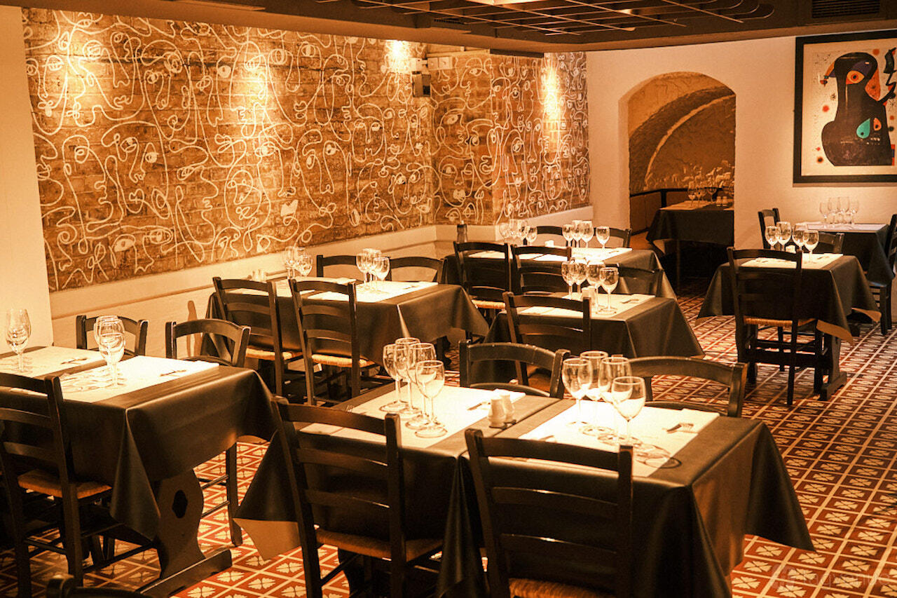 A restaurant dining area with dark wooden chairs, patterned tile floors, and abstract wall art at El Pirata of Mayfair.