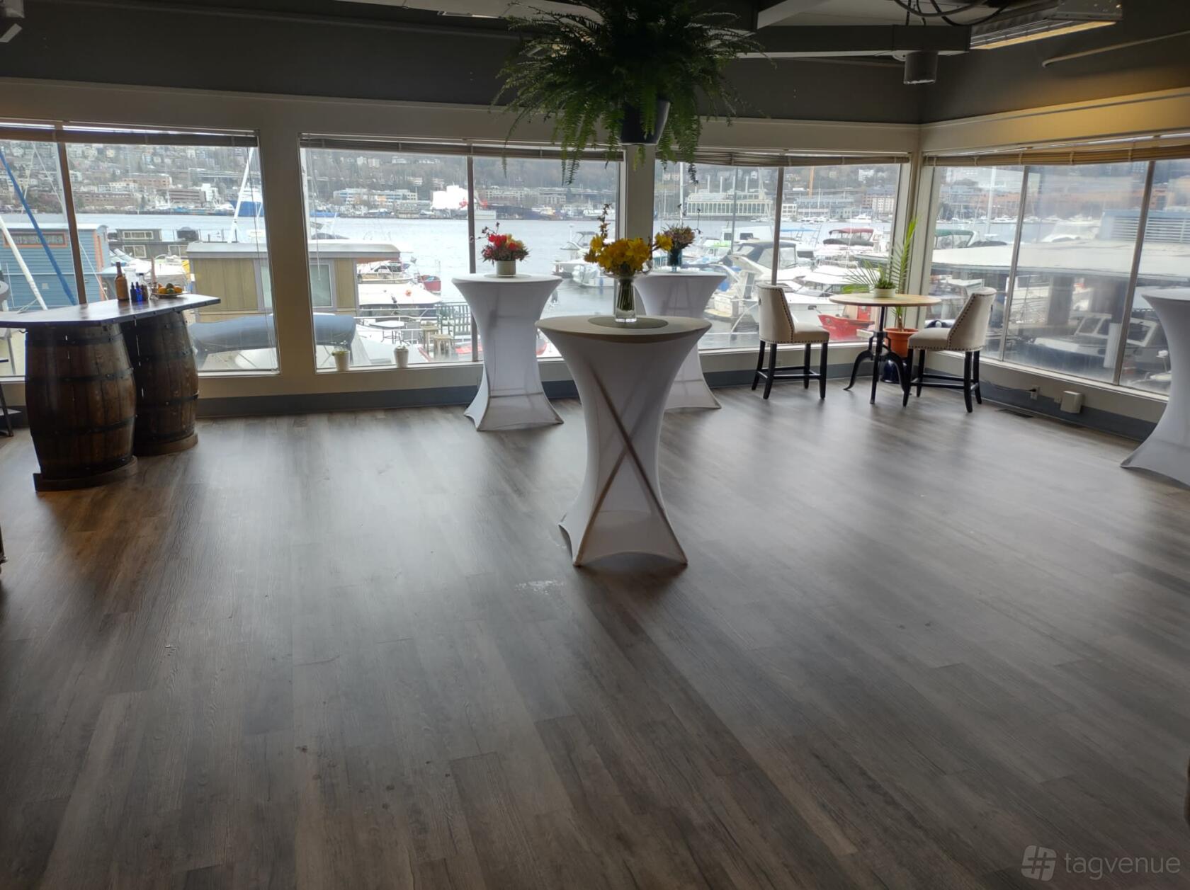 An event space with floor-to-ceiling windows overlooking a marina, cocktail tables, and wood flooring at Seattle Bartending Co.