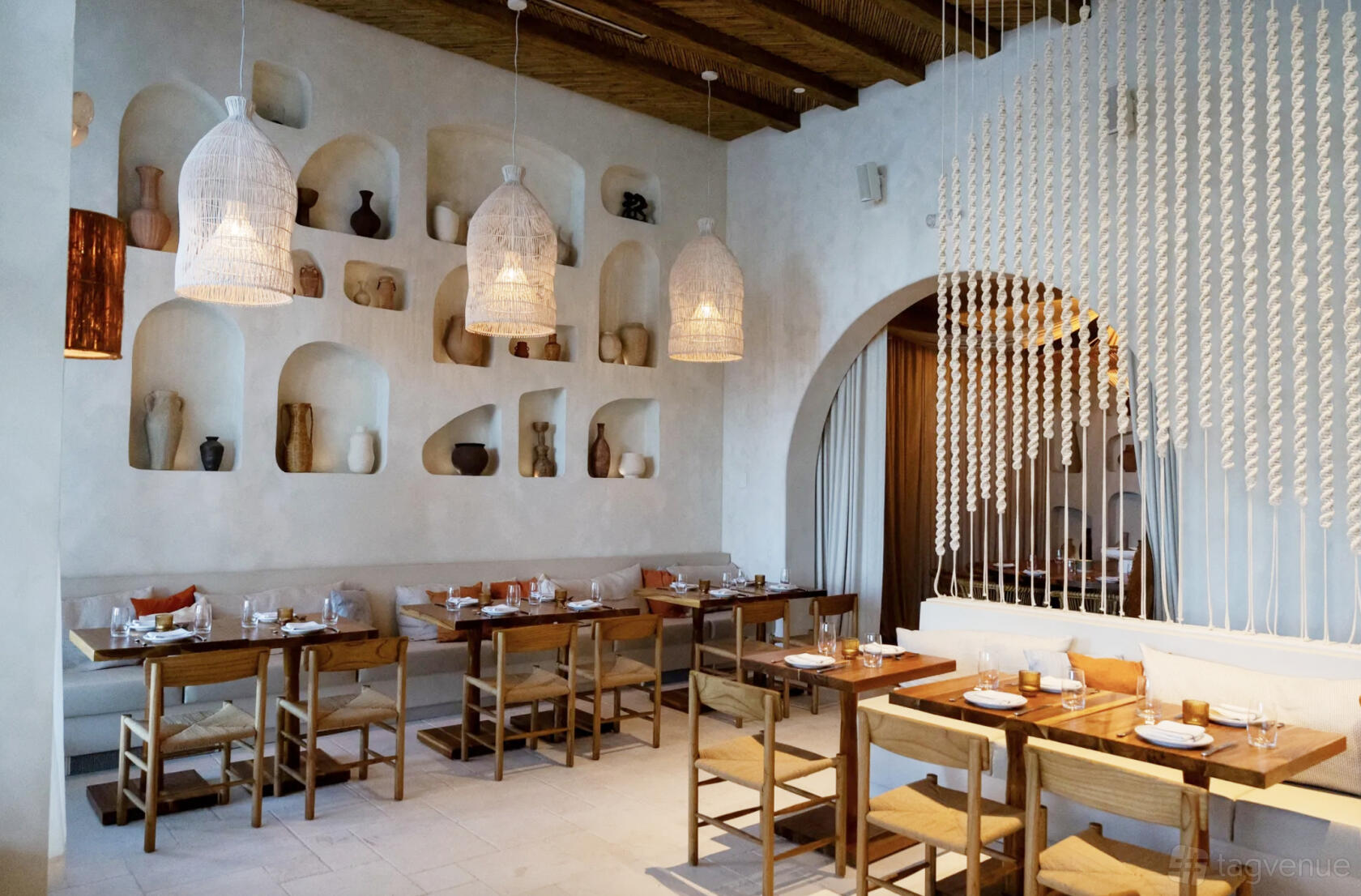 An event space in a restaurant with woven pendant lights, wooden tables, and decorative alcove shelving at Yaya Coastal Cuisine.