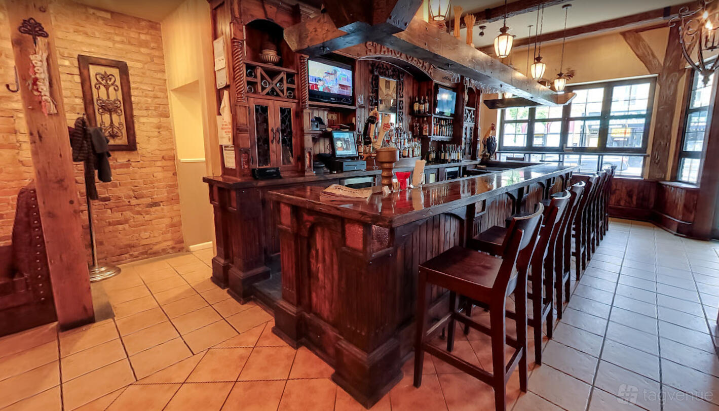 A bar in a restaurant with a polished wood counter, high-backed chairs, and exposed ceiling beams at Staropolska Restaurant.