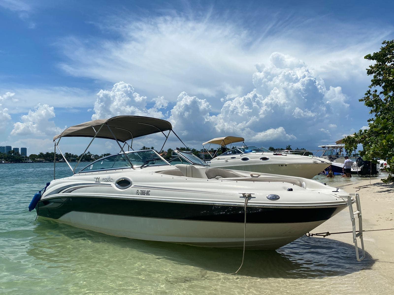 A white deck boat with a tan canopy anchored on a sandy shoreline at 26' Sea Ray 240 Sundeck Experience.