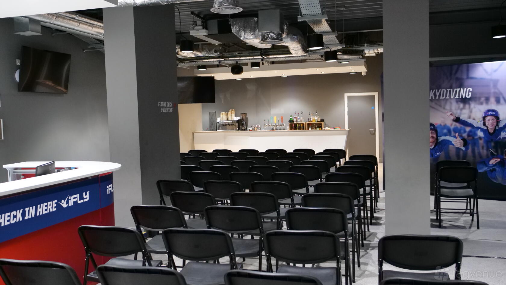 A meeting room with rows of black chairs facing a bar counter stocked with drinks at iFLY Indoor Skydiving at The O2.