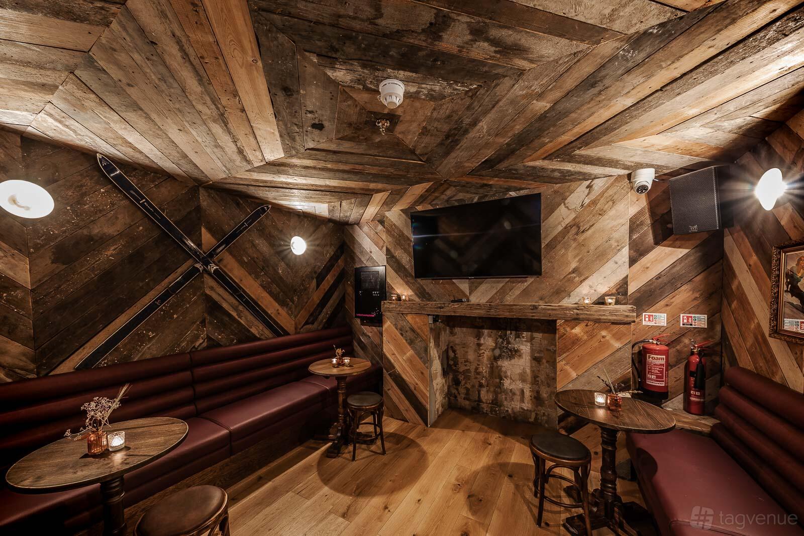 A karaoke room with wood-paneled walls, a mounted TV, round tables, and banquette seating at Queen of the South.