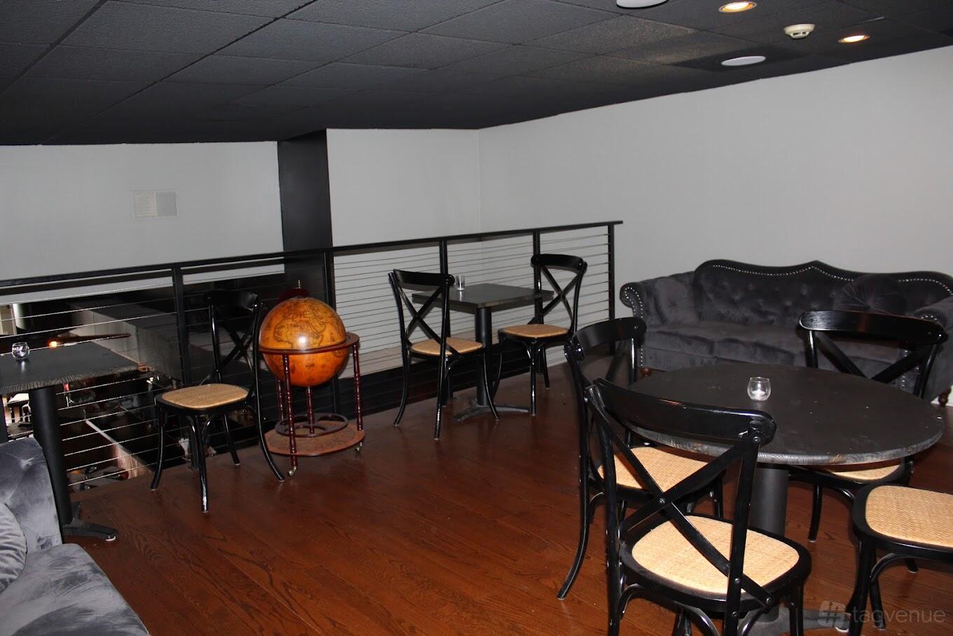 An upstairs restaurant lounge with dark wood floors, black sofas, round tables, and a decorative globe at Newbolds Food & Libations.