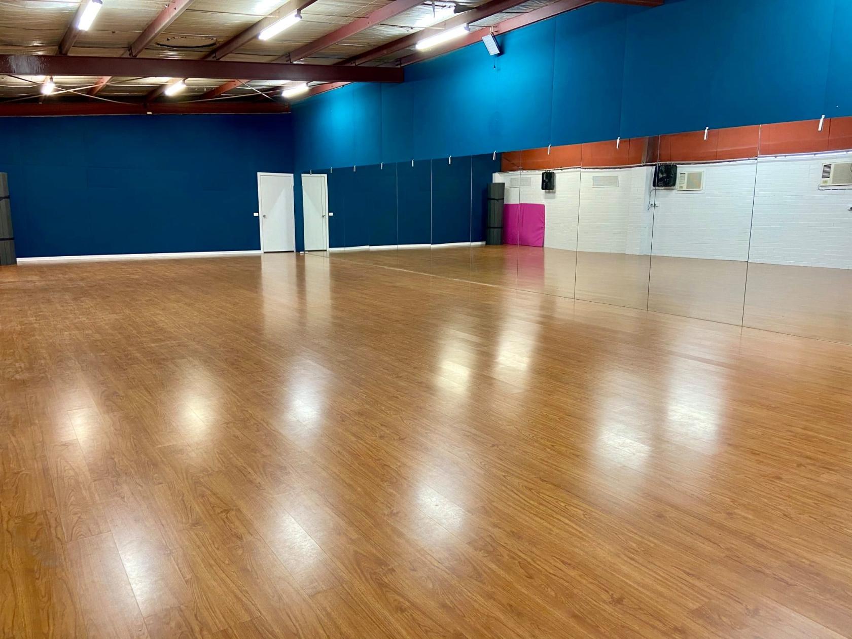 A dance studio with wood flooring, mirrored walls, and blue accent walls at National Performing Arts Company.