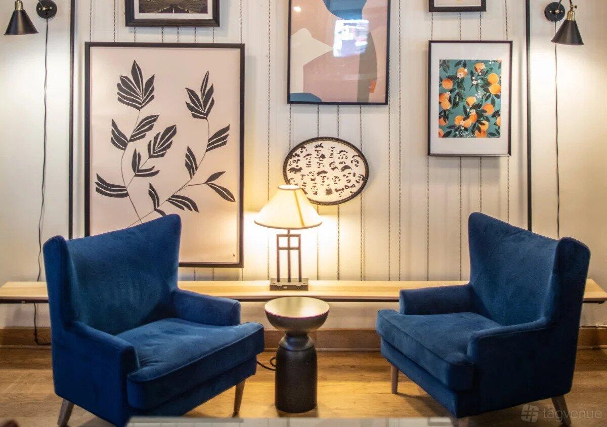 An event space in a cafe with blue velvet armchairs, framed artwork, and warm accent lighting at Three Whistles - Eat Drink Work.