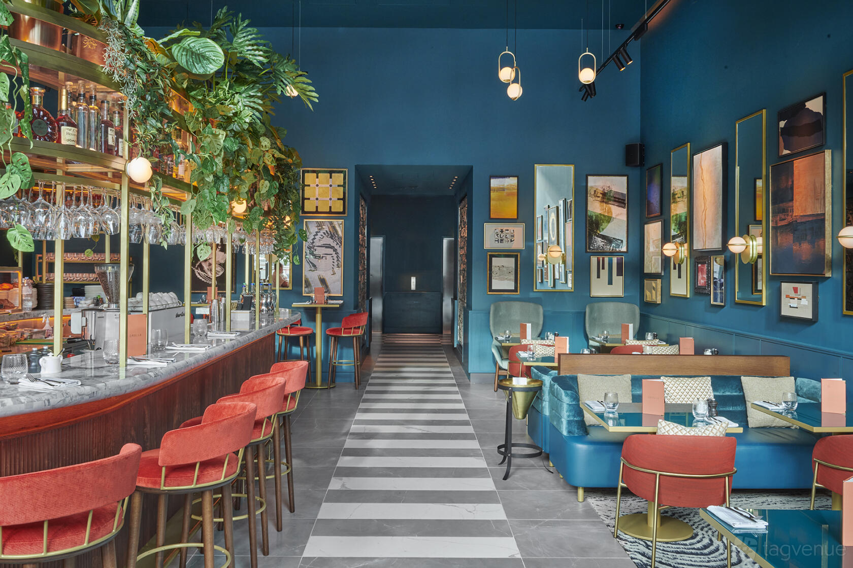 An event space in a restaurant with a marble bar, red velvet stools, vibrant blue walls, and framed artwork at Orelle.