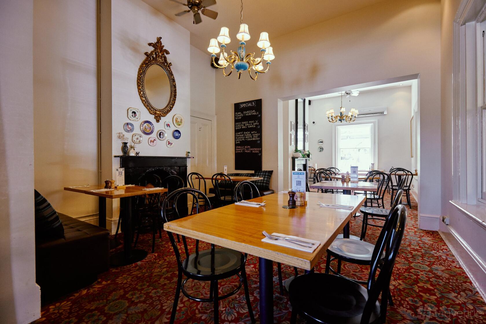 A restaurant with wooden tables, black chairs, chandeliers, and vintage decor at The Mint Bar & Restaurant.