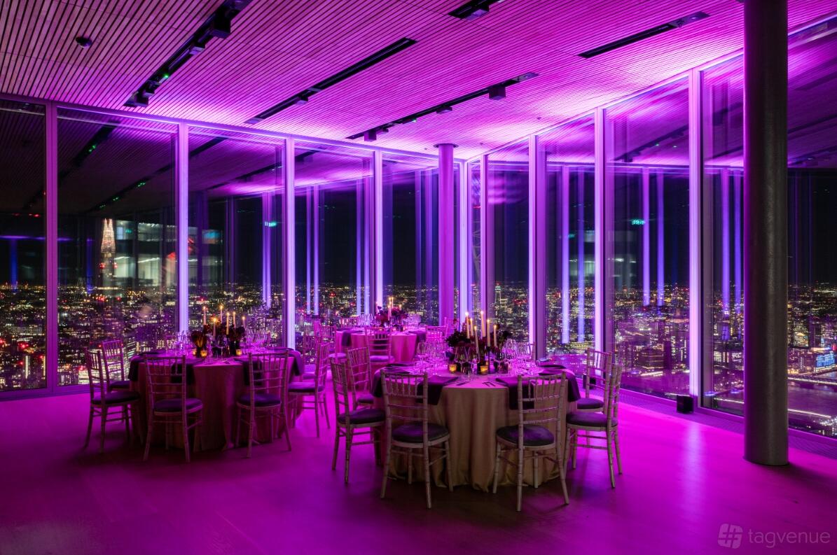 An event venue with floor-to-ceiling windows, round tables with candles, and purple lighting at 8 Bishopsgate.