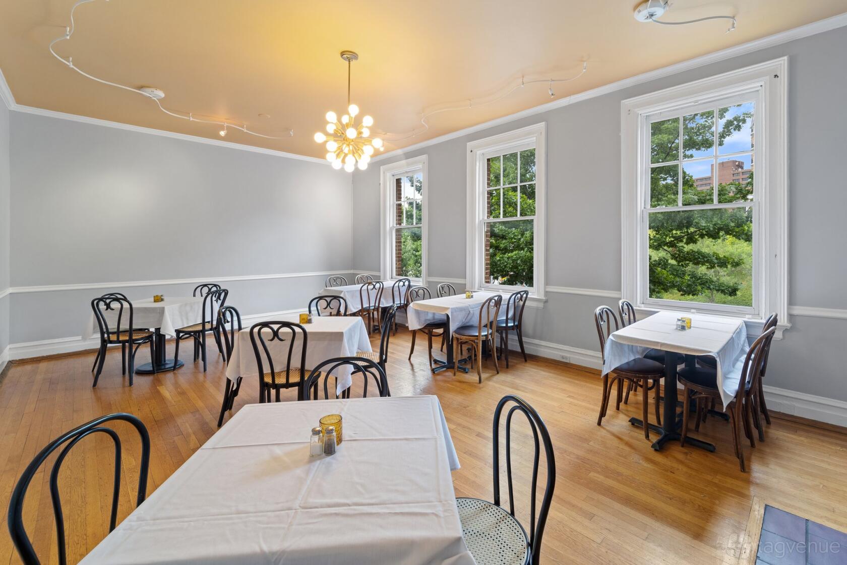 A dining room with large windows, wood floors, and square tables with white tablecloths at Petit Monde Cafe.