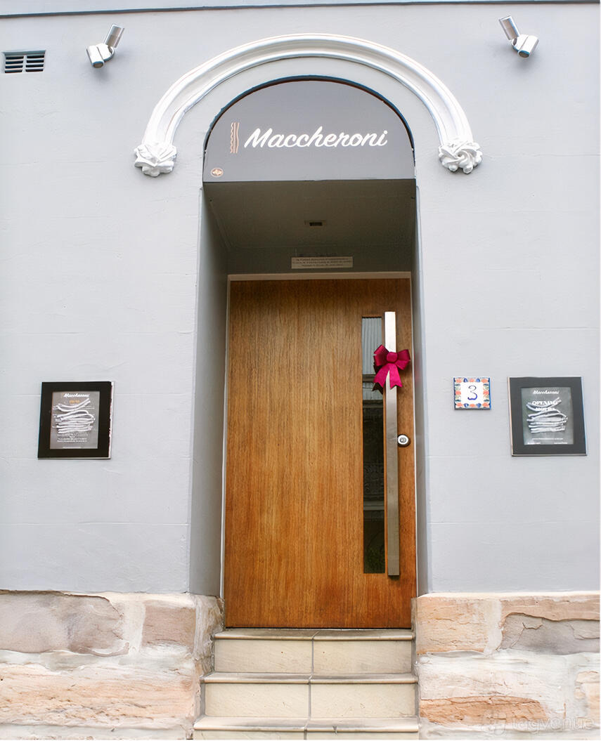 A restaurant entrance with a wooden door, red ribbon decoration, and framed menus at I Maccheroni Restaurant.