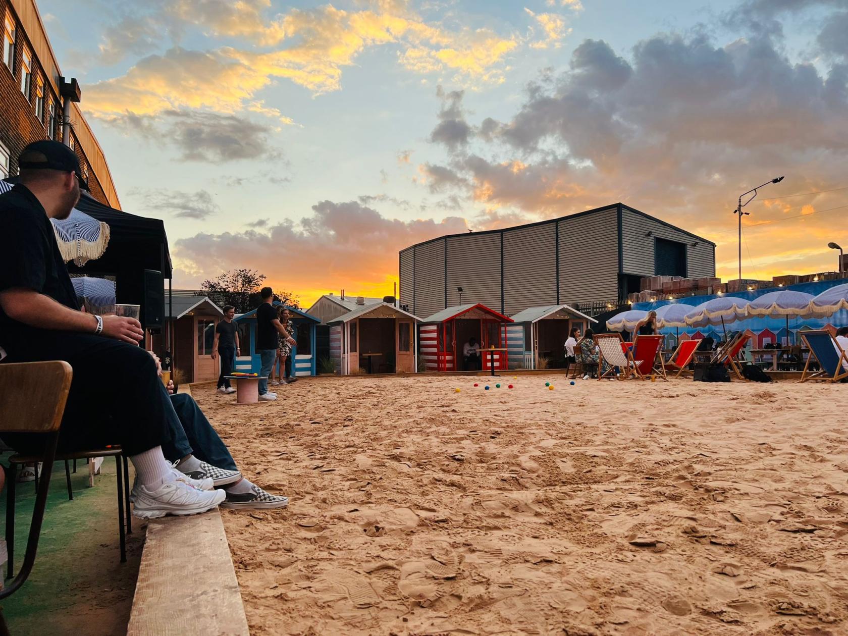 An outdoor event space with a sandy area, colorful beach huts, and deck chairs at Big Penny Social.