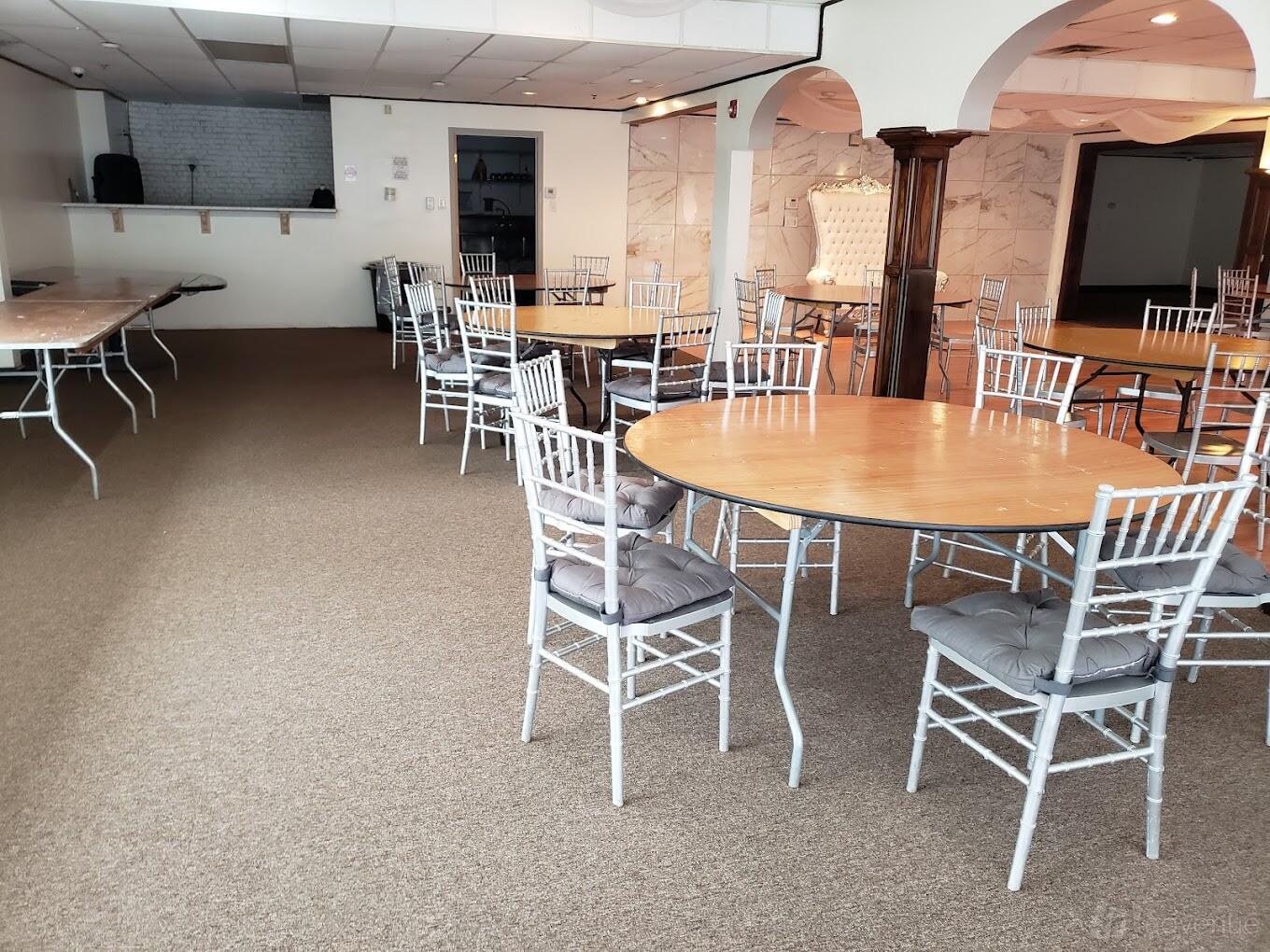 An event venue with round wooden tables, silver chiavari chairs, and carpeted floors at Visions Event Center.