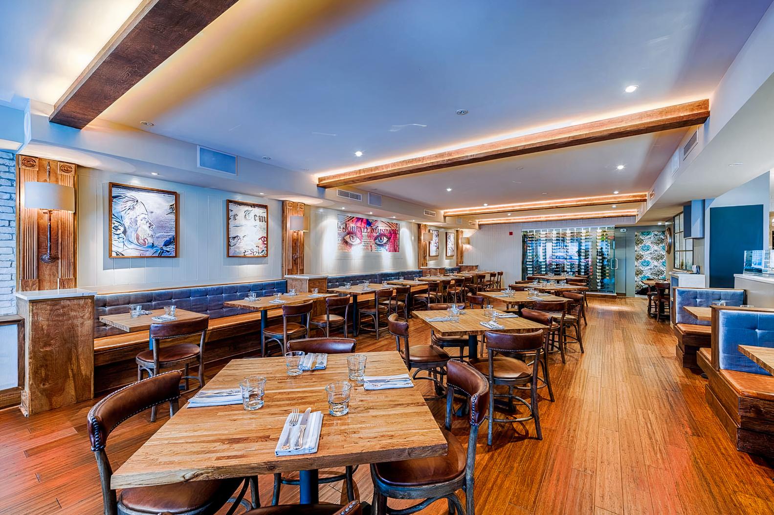A restaurant with wood floors, wooden tables, blue banquette seating, and modern art on the walls at Le DeSales.