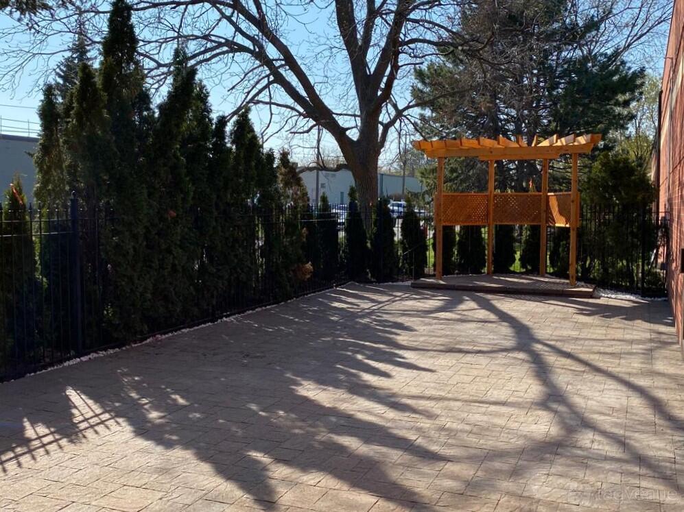 An outdoor patio with brick paving, evergreen trees, and a wooden pergola at Renaissance by the Creek.