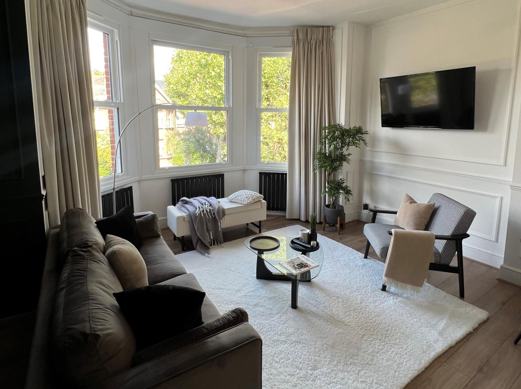A photo studio with a large bay window, neutral furnishings, and a plush white rug at Laurent’s Living Room.