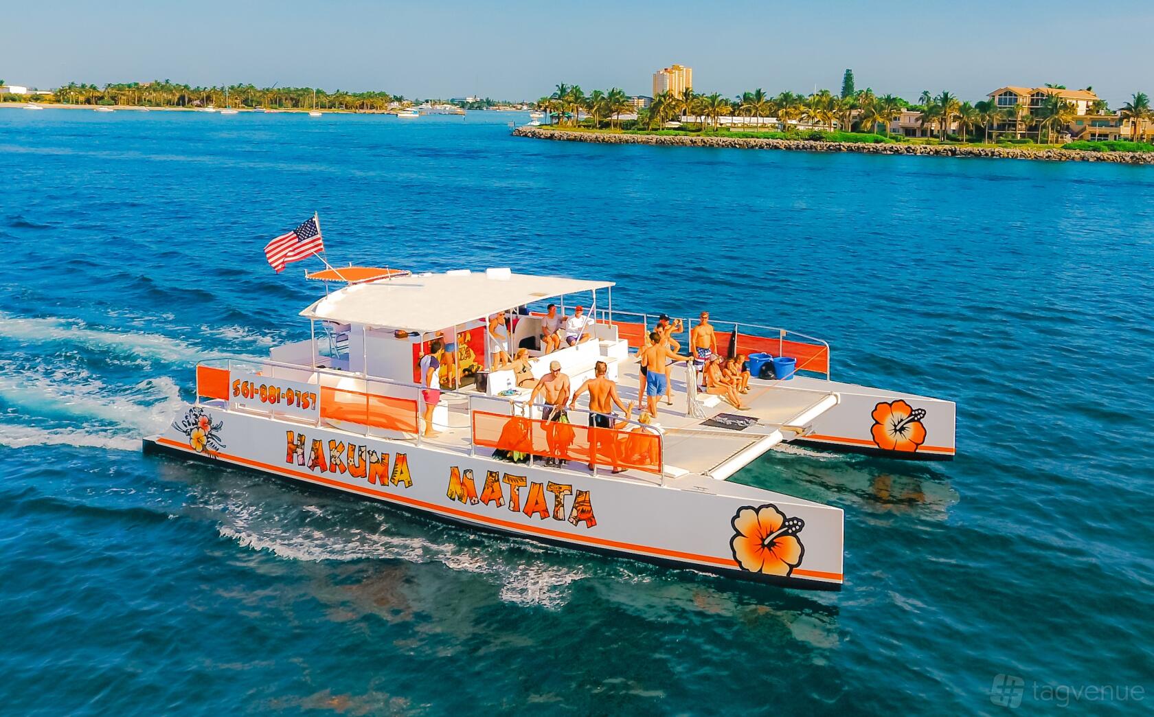 A party boat with open-air deck, orange floral accents, and guests enjoying the sun on Hakuna Matata by Lots Of Yachts/Lots Of Spots South Florida.