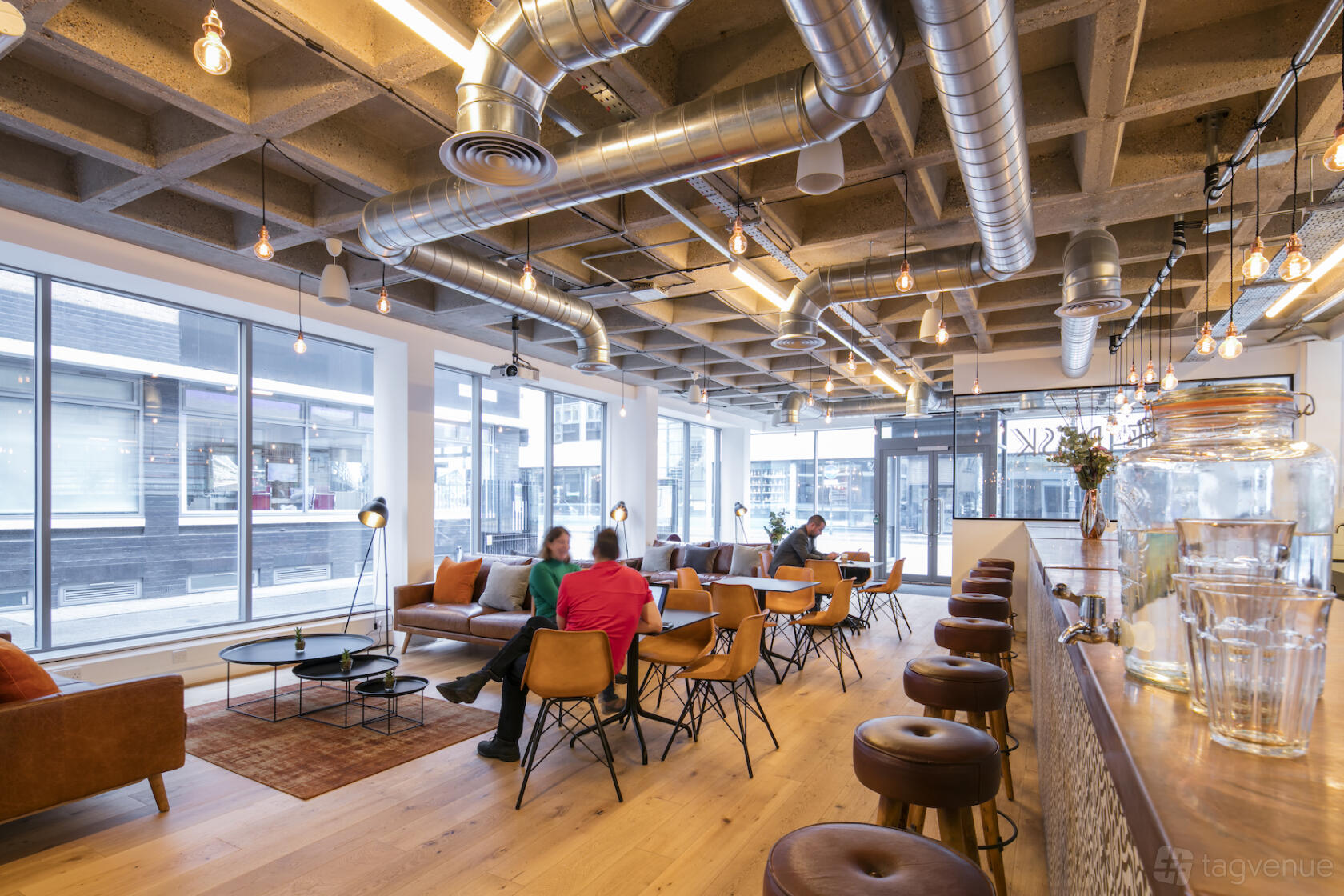 An event space with exposed ductwork ceilings, floor-to-ceiling windows, and mixed lounge seating at Curtain Road.