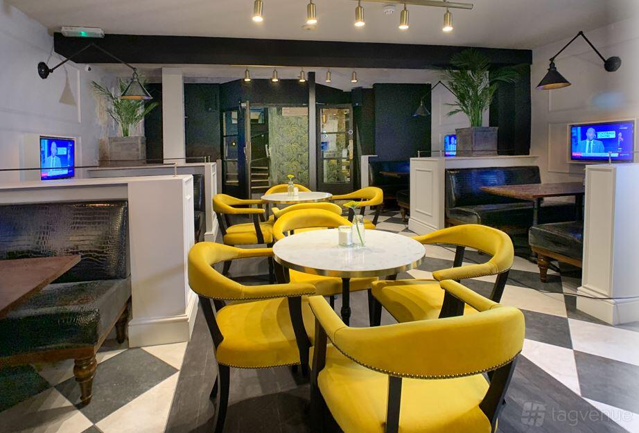 A lounge with yellow upholstered chairs, marble-top tables, and black booths at Bonds