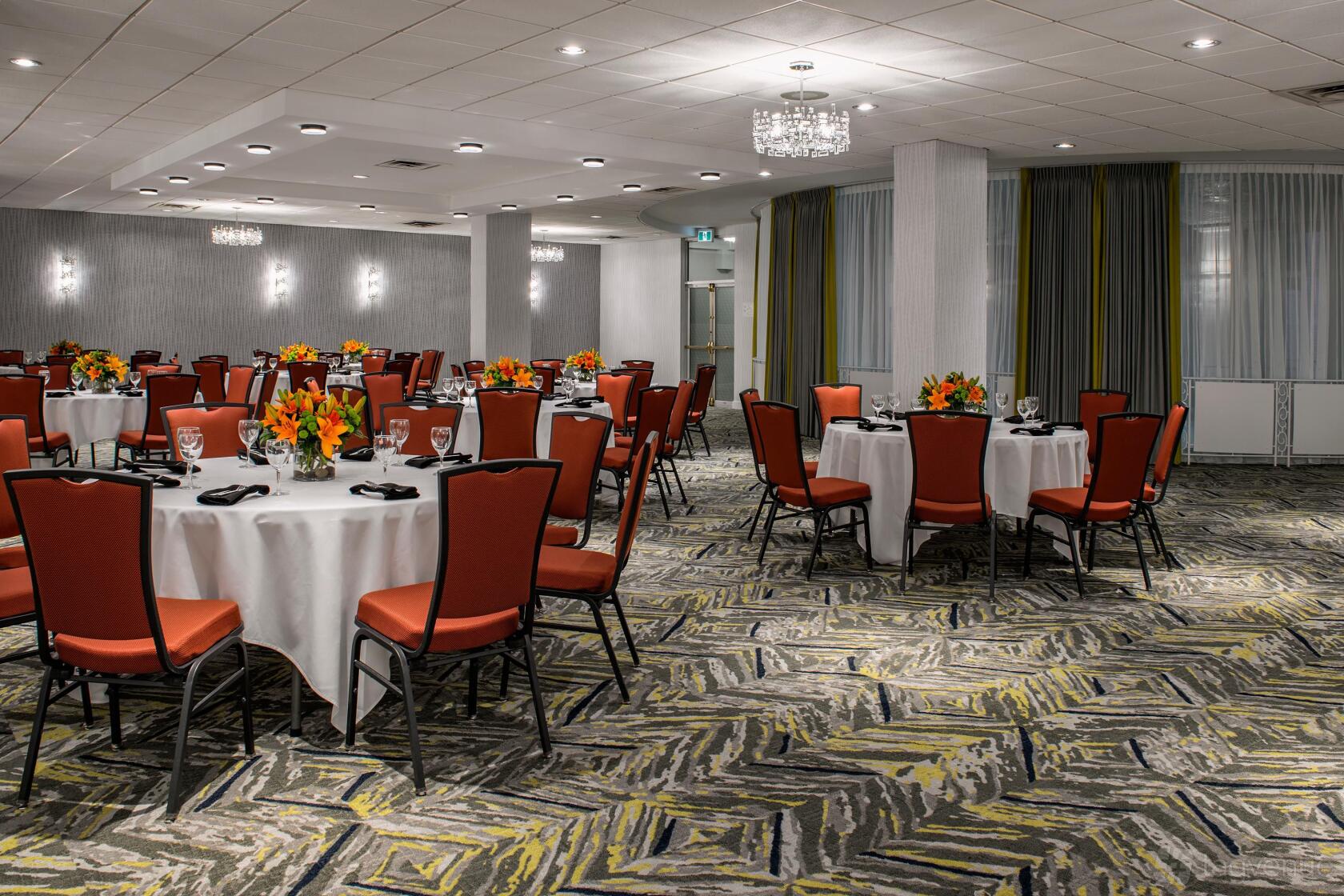 A function room with round tables set with white linens, orange chairs, and floral centerpieces at Holiday Inn & Suites Vancouver Downtown.
