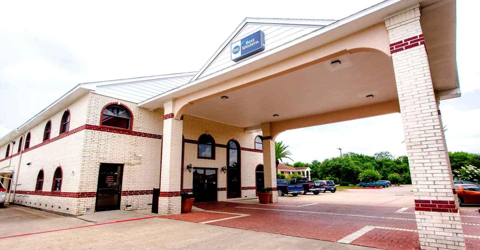 A hotel entrance with white brick columns, a covered driveway, and arched windows at Best Western Pearland Inn.