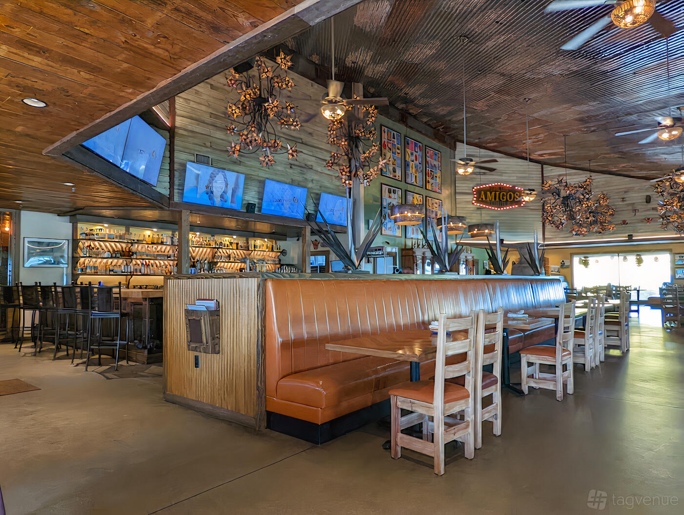 A restaurant with wooden tables, tan leather booths, hanging pendant lights, and a bar with high stools at Taco Grande.
