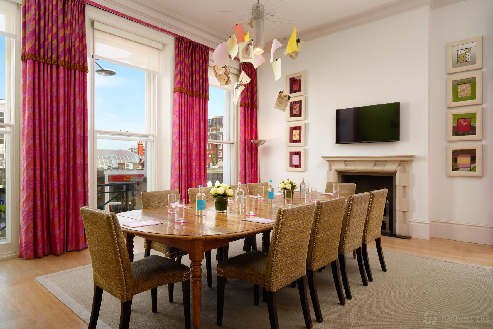 A hotel meeting room with a long wooden table, wicker chairs, large windows, and colorful curtains at The Pelham Hotel.