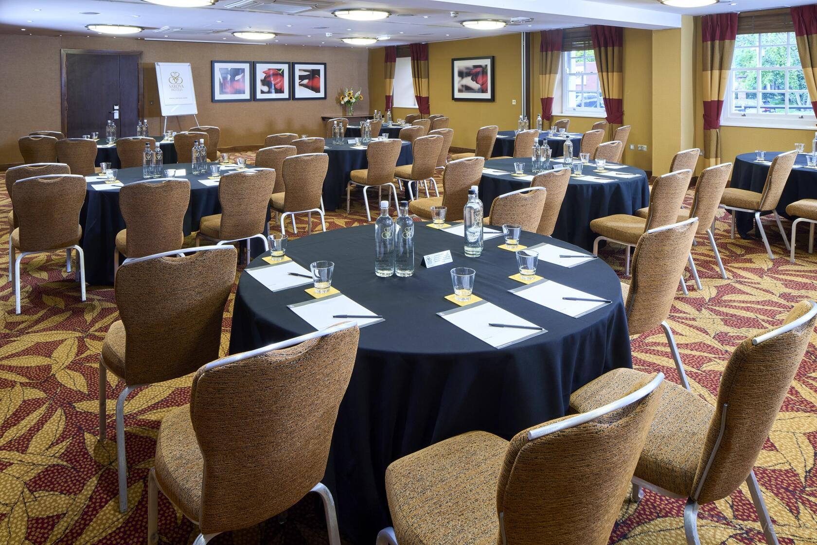A meeting room with round tables covered in black linens and natural light from large windows at The Bull Hotel.