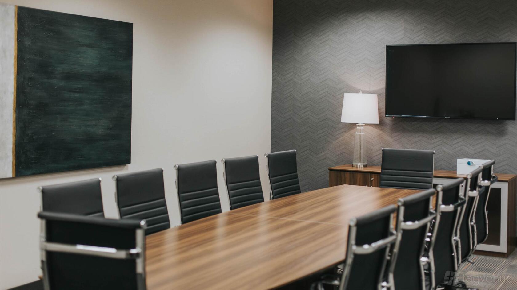 A coworking space with a long wooden conference table, black leather chairs, wall-mounted TV, and lamp at Executive Workspace Preston Center.