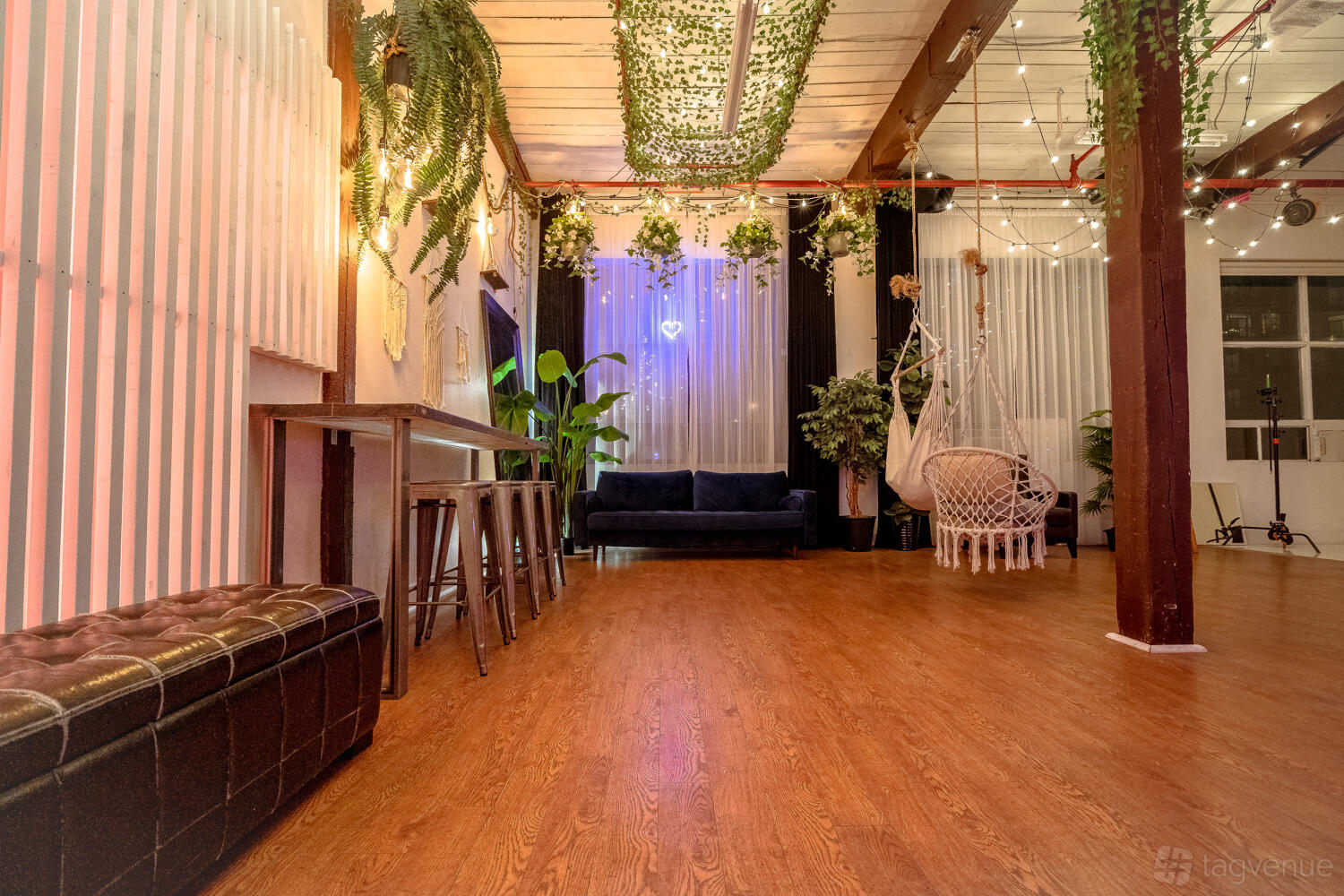 A loft with wood flooring, hanging plants, string lights, and a navy sofa at Daylight Studio for Photos, Events, Meetings.