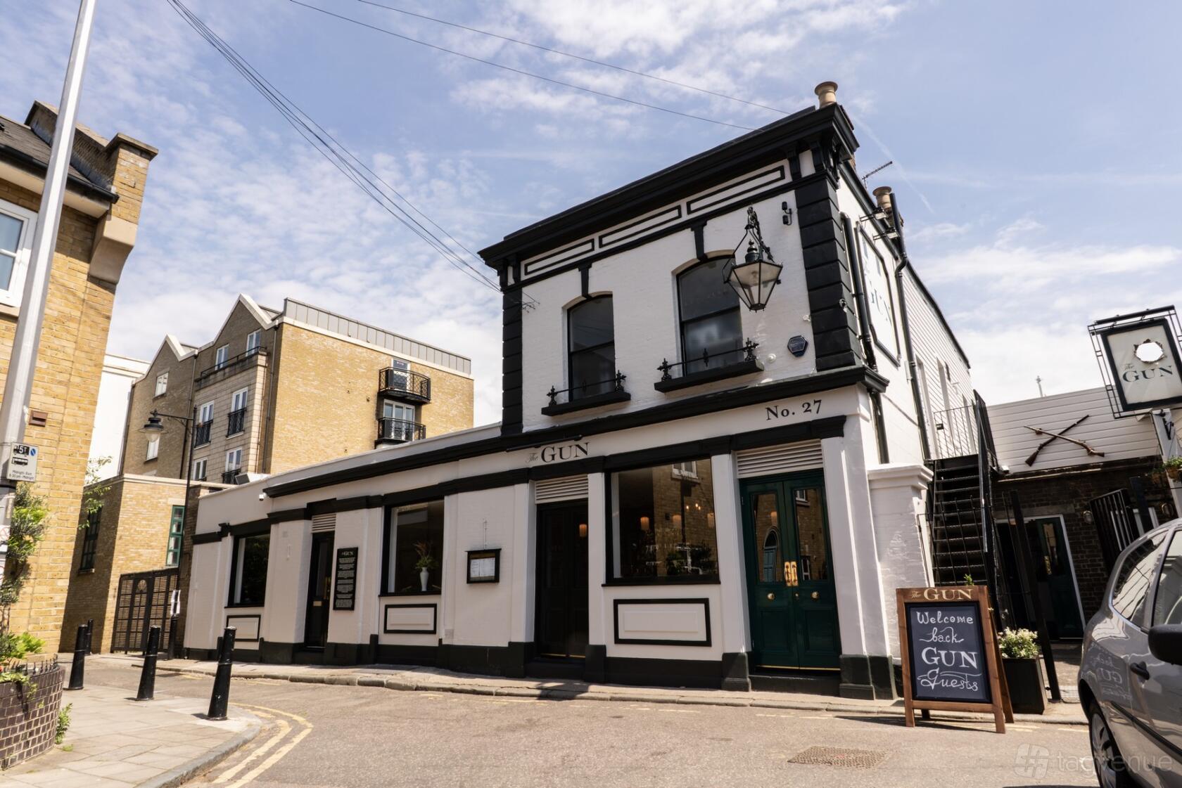 A corner pub with white and black facade, large windows, and a hanging lantern at The Gun.