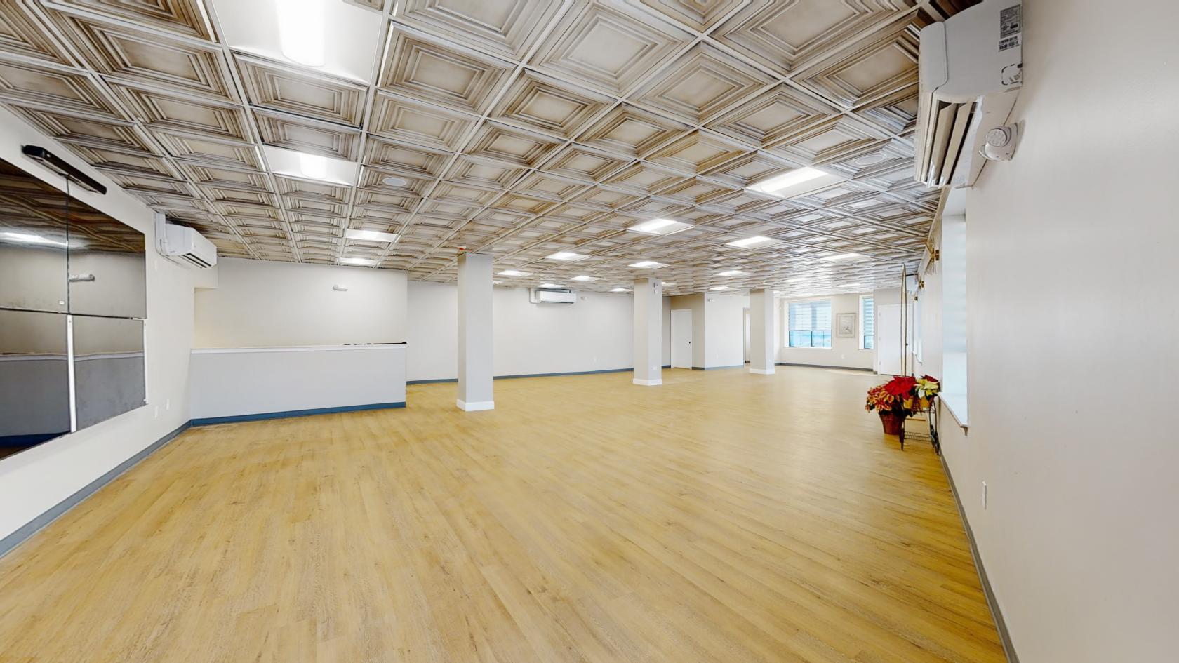 An event space with wood flooring, coffered ceiling tiles, pillars, and large windows at Jenice's Event & Conference Center.