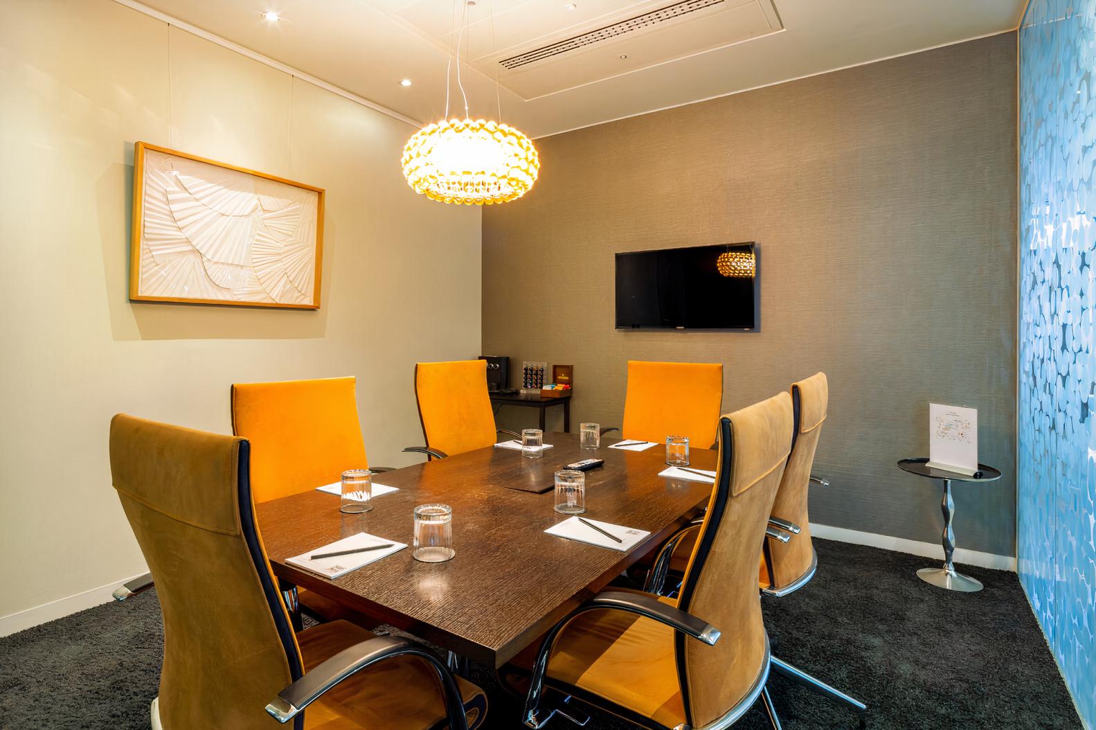 A meeting centre with a rectangular table, yellow high-back chairs, and a wall-mounted TV at Landmark: Heron Tower, London.