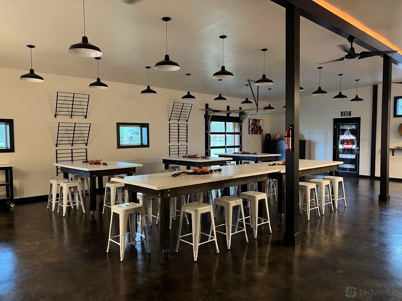 An event venue with long work tables, white stools, hanging ceiling lights, and dark polished floors at HUB510.