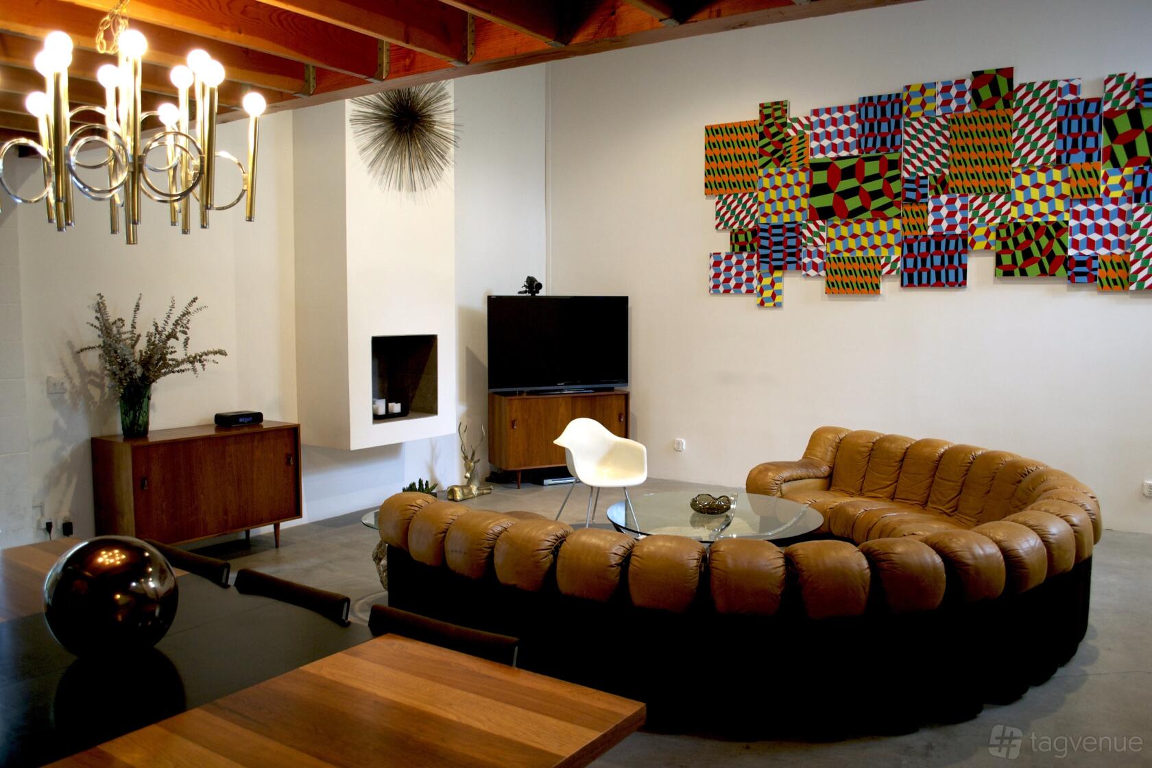 A loft with exposed wood beams, a curved leather sofa, abstract wall art, and mid-century furnishings at Large Creative Venice Loft Space.