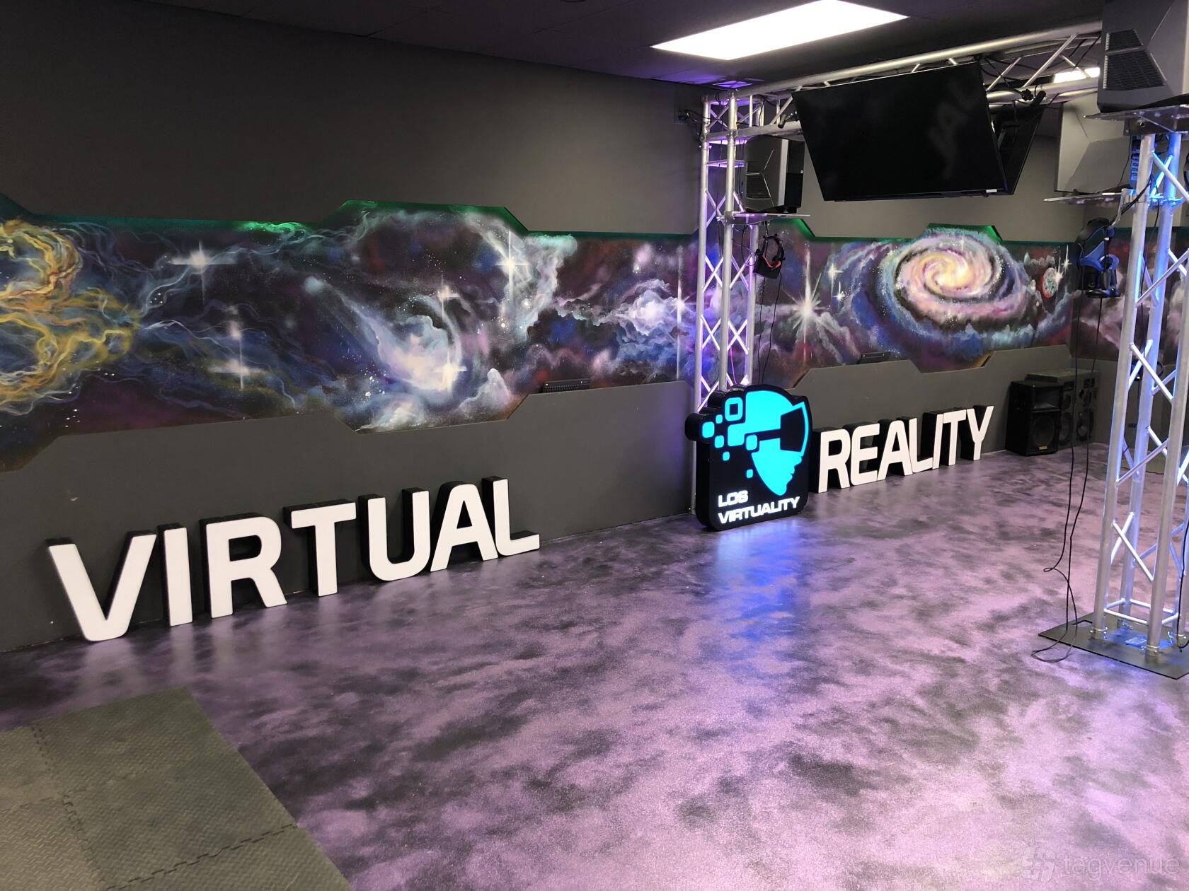 An art studio with galaxy-themed wall murals, metallic floor, and a neon logo sign at Los Virtuality - VR Arcade - Los Angeles.
