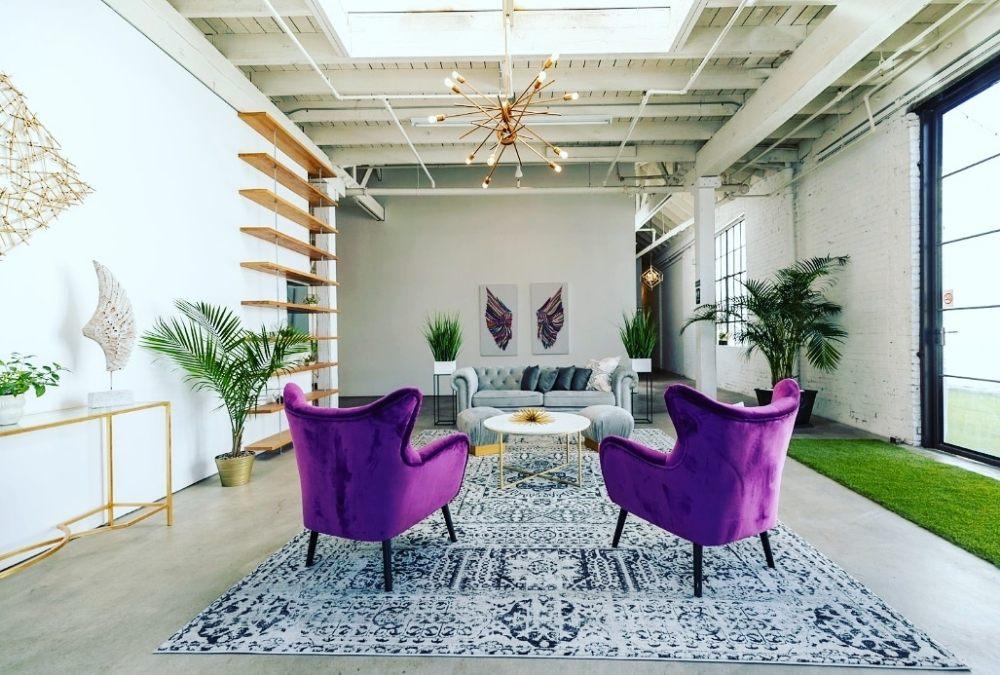 An event venue foyer with skylights, purple armchairs, a patterned rug, and indoor plants at The East Angel.
