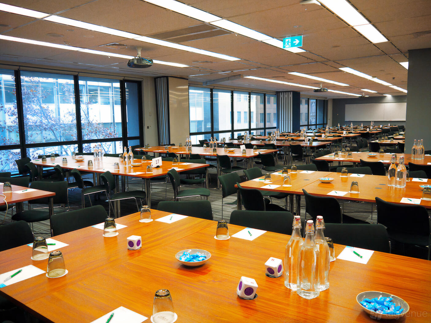 A conference room with large windows, wooden tables set with water bottles and notepads at Cliftons Sydney Spring St.
