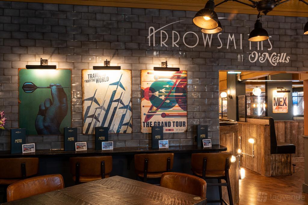 An event space in a pub with dart-themed wall art, exposed brick tiles, and wooden tables at Arrowsmiths @ O'Neill's Solihull.