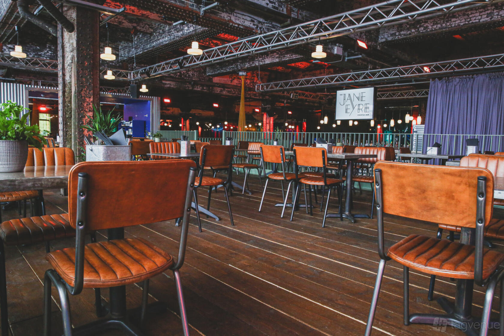 A covered terrace with wooden flooring, leather chairs, potted plants, and exposed steel beams at Escape To Freight Island.
